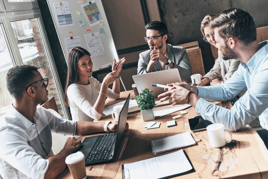 A group of people sitting around a table with laptops open cooperating to achieve a common goal.